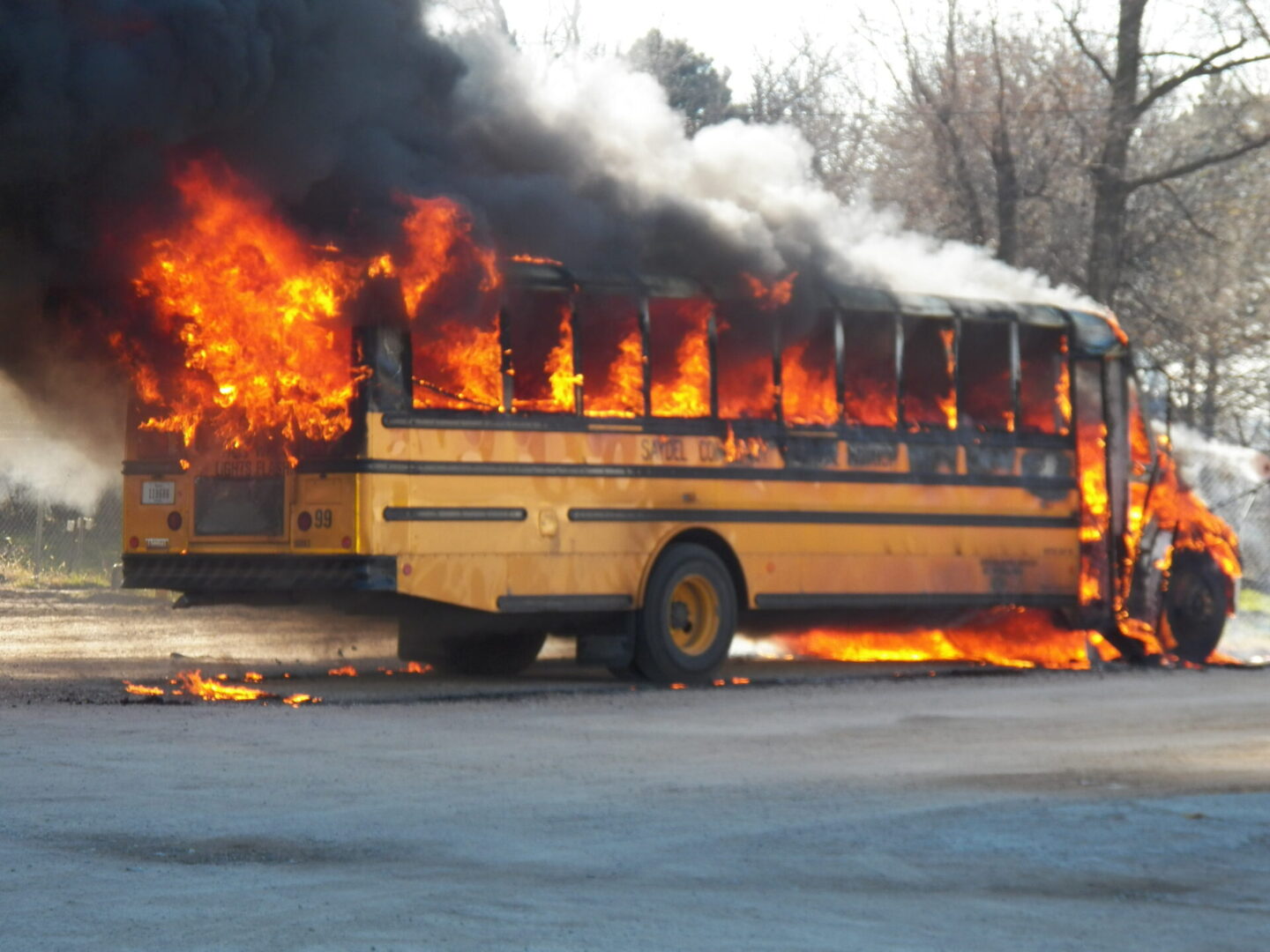 A school bus is burning on the side of the road.